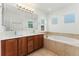 A bathroom featuring dual sinks, wood cabinets, a large soaking tub, and a window at 10618 Clearview Ln, Highlands Ranch, CO 80126