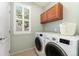 A laundry room with a white washer and dryer, wood cabinets, and a bright window at 10618 Clearview Ln, Highlands Ranch, CO 80126