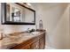Stylish half bath features a granite countertop, a wooden vanity, and a large framed mirror at 6963 S Espana Way, Centennial, CO 80016