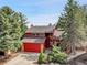 This exterior shot showcases a red two-story home with mature trees and landscaping at 15740 Sandtrap Way, Morrison, CO 80465