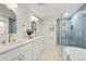 Modern bathroom featuring dual sinks, a luxurious soaking tub, and a glass-enclosed shower with blue accent tiles at 7382 W Stanford Ave, Littleton, CO 80123