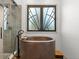 Luxurious bathroom showcasing a copper soaking tub with a sleek faucet and a mosaic tiled shower, illuminated by a unique frosted window at 34427 Columbine W Trl, Elizabeth, CO 80107