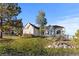 Tan single-story house on a lush green lawn featuring a stone retaining wall and scattered trees under a clear blue sky at 34427 Columbine W Trl, Elizabeth, CO 80107