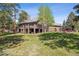 Large backyard featuring mature trees, green grass, a two-story deck, and lovely stone retaining wall at 1570 Blakcomb Ct, Evergreen, CO 80439