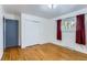 Bright bedroom features a window with red curtains, hardwood floors, closet, and access door at 8511 Essex Dr, Denver, CO 80229