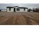 Exterior view of the house with fresh white paint, black trim, gray gravel, a propane tank, and tire tracks at 7486 Harold St, Fort Lupton, CO 80621