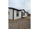 The exterior side view of the house with fresh white paint and black trim, landscaping rocks, and a small porch at 7486 Harold St, Fort Lupton, CO 80621