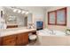 Bright bathroom featuring a soaking tub next to a fireplace, vanity, and a large mirror with great lighting at 5350 S Marshall St, Littleton, CO 80123