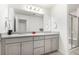 Elegant bathroom featuring double vanity with sleek gray cabinetry, granite countertops, and a glass-enclosed shower at 803 N Bently St, Watkins, CO 80137