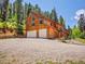 Exterior of a beautiful two-story wooden home with two-car garage surrounded by mature trees at 11768 Black Hawk Dr, Conifer, CO 80433