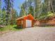 Exterior of a wooden outbuilding with a white garage door surrounded by mature trees at 11768 Black Hawk Dr, Conifer, CO 80433
