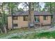 Exterior back view of tan home with brick chimney, surrounded by mature trees, and deck access stairs at 9416 Mcshane Ct, Parker, CO 80134