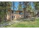 View of back of tan home with brick chimney, surrounded by mature trees, plus wooden deck with access stairs at 9416 Mcshane Ct, Parker, CO 80134