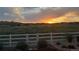 Serene backyard view of a grassy field with white fence silhouetted against a dramatic sunset sky at 6070 Long Branch Dr, Parker, CO 80134