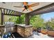 A comfortable outdoor kitchen and patio under the pergola features a grill, stone counter, and many plants and trees at 7243 S Kellerman Way, Aurora, CO 80016