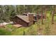 Exterior view of the home featuring a stone chimney, wood siding, deck, and lush natural surroundings, blending with nature at 3251 Interlocken Dr, Evergreen, CO 80439
