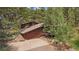 View of the front exterior with a driveway and attached garage surrounded by trees, stone walls, and natural landscaping at 3251 Interlocken Dr, Evergreen, CO 80439