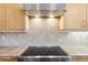 Close up of stovetop and tile backsplash in kitchen with wooden cabinets and stainless hood at 6743 Serena Ave, Castle Pines, CO 80108