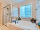 Modern bathroom featuring a soaking tub with tile surround, a glass-enclosed shower, and a bright window at 607 Azalea St, Brighton, CO 80601