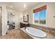 Bright bathroom featuring a soaking tub, dark wood vanity, and a large window with scenic views at 7172 S Oakleaf St, Bennett, CO 80102