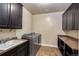 Functional laundry room featuring modern washer/dryer, sink, and dark cabinets for storage at 7172 S Oakleaf St, Bennett, CO 80102