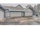 Three-car garage with gray siding and blue trim, showing the garage door and driveway in winter at 2504 S Victor St # E, Aurora, CO 80014