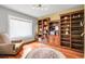 Cozy home office featuring custom built-in bookshelves, hardwood floors, a large window, and a comfortable armchair at 11411 W Cooper Dr, Littleton, CO 80127