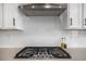 Close-up of the gas cooktop with a stainless steel hood and white backsplash for modern cooking at 1408 Brookfield Pl, Lafayette, CO 80026