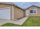 Tan home featuring an attached garage, well-kept lawn, and attractive front entrance at 664 Stampede Dr, Brighton, CO 80603