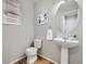 Cozy powder room featuring wood floors, pedestal sink, and a charming round mirror at 15047 E 50Th Dr, Denver, CO 80239