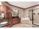 Well-lit bathroom featuring wood cabinetry, a jacuzzi tub, and glass shower with tile surround at 20097 Royal Troon Dr, Monument, CO 80132