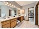 Well-lit bathroom with dual sinks, wood cabinets, and a view into the main bedroom at 3487 Willownook Ranch Trl, Elizabeth, CO 80107