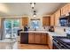 Well-lit kitchen with wood cabinets, black appliances, and sliding door access to backyard patio at 11395 E 116Th Dr, Commerce City, CO 80640