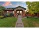 Charming brick home featuring a covered front porch, manicured lawn, and lush landscaping at 1215 Jackson St, Denver, CO 80206