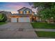 Charming home featuring a three-car garage, well-lit exterior, and landscaped front yard under a colorful evening sky at 10723 W 54Th Pl, Arvada, CO 80002