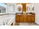 Bathroom with tub, wood cabinets, tile flooring, oval mirrors, and decorative tile backsplash at 2412 Windmill Dr, Longmont, CO 80504