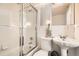 A white tiled bathroom with an updated shower, pedestal sink, and stylish guitar accent lamp at 1946 Ensenada St, Aurora, CO 80011