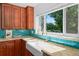 Farmhouse sink nestled under window, wood cabinets, granite counters, and blue tile backsplash at 3001 S Josephine St, Denver, CO 80210