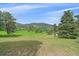 Expansive green property with scattered trees and a distant house against a backdrop of rolling hills at 9745 Hilldale Dr, Morrison, CO 80465