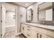 Bright bathroom offers double sinks with white cabinets, framed mirrors and tiled shower/tub with gray wood-look flooring at 14952 Vienna Cir, Parker, CO 80134