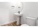 Modern powder room featuring a pedestal sink, round mirror, black hardware, and wood-look flooring at 5785 N Jericho Way, Aurora, CO 80019