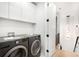 Bright laundry room features side-by-side washer and dryer, white cabinets, and hardwood floors leading to stairs at 1823 W 35Th Ave, Denver, CO 80211