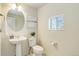 Bright half-bath with pedestal sink, round mirror, toilet, and window with blinds at 9180 E 52Nd Dr, Denver, CO 80238