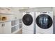 Modern laundry room with white front-load washer and dryer, built-in shelving, and ample countertop space at 14337 Shasta Daisy Pt, Parker, CO 80134
