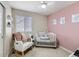 Cozy Bedroom with a white crib, rocking chair, pink accent wall and natural light from the window at 17265 E 110Th Ct, Commerce City, CO 80022