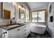 Well-lit bathroom featuring a white vanity, modern bathtub, a stylish mirror, and a window for natural light at 1295 Hy Vu Dr, Evergreen, CO 80439