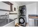 Bright laundry room with stainless steel sink, floating shelves, and stacked, front-loading, dark-colored washer/dryer at 1108 Roslyn St, Denver, CO 80220