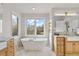 Beautiful bright bathroom featuring wood cabinets, marble countertops, soaking tub, and stylish fixtures at 31699 Southern Hills Pl, Evergreen, CO 80439