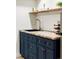 This bar area features blue cabinets, a wooden countertop, gold hardware and faucet, and decor on an open shelf at 3100 S Holly Pl, Denver, CO 80222