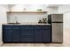 This bar area features blue cabinets, a wooden countertop, a mini fridge, and decor on an open shelf at 3100 S Holly Pl, Denver, CO 80222